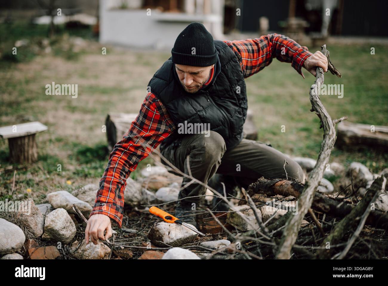 Der Mann sammelt Stöcke und Steine an einer Feuerstelle im Hinterhof Stockfoto