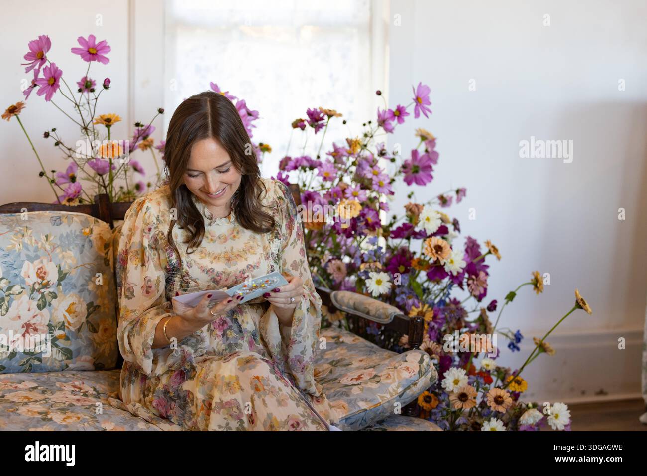 Eine Frau auf Blumensofa, umgeben von Blumen, liest eine Karte Stockfoto