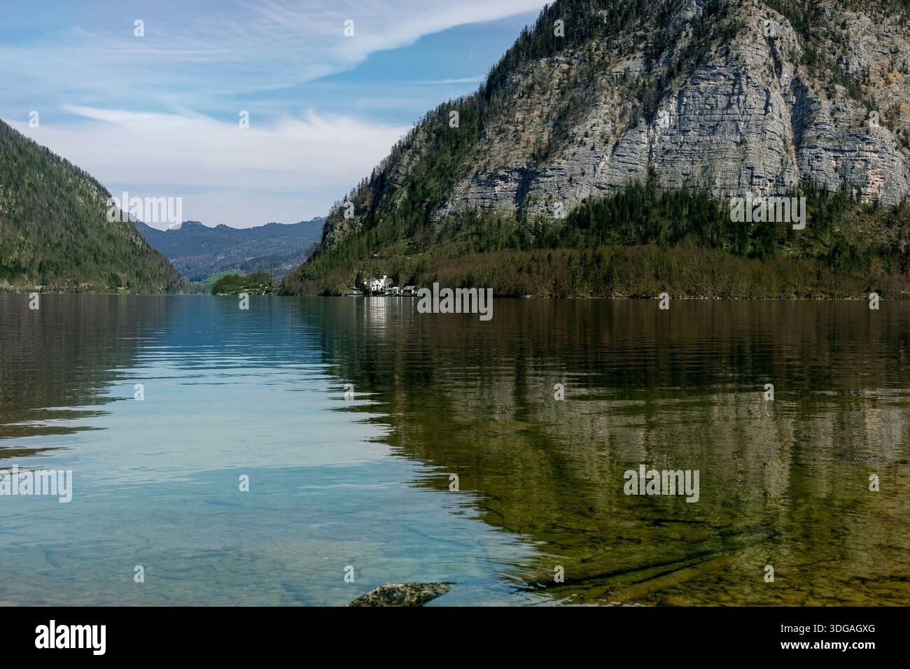 Hallstatt Österreich. Ruhiger Bergsee umgeben von steilen Bergketten, die sich in klarem türkisfarbenem Wasser spiegeln. Kleine Siedlung sichtbar an der Küste. Stockfoto