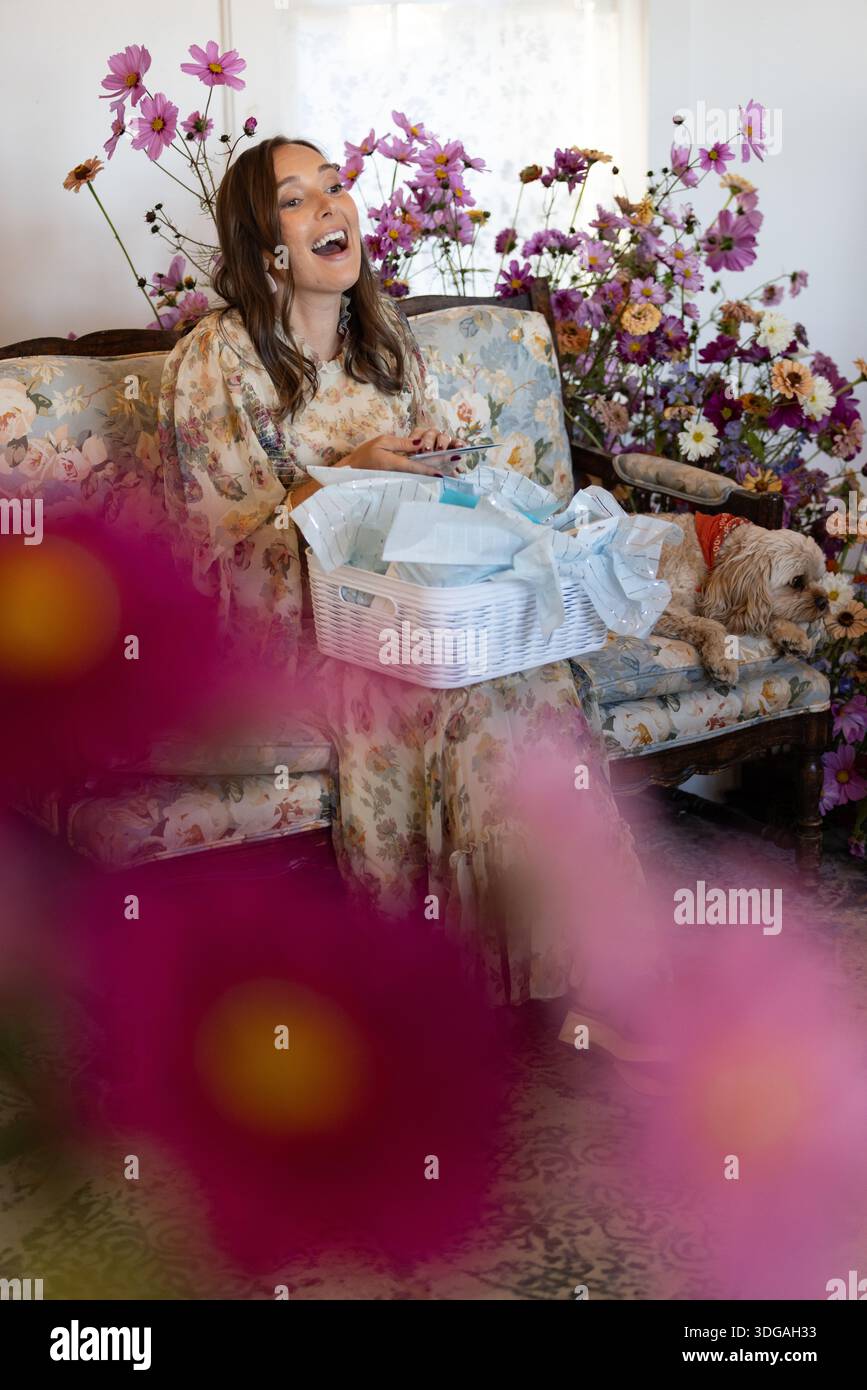 Frau lacht, während sie eine Karte und einen Geschenkkorb öffnet Stockfoto