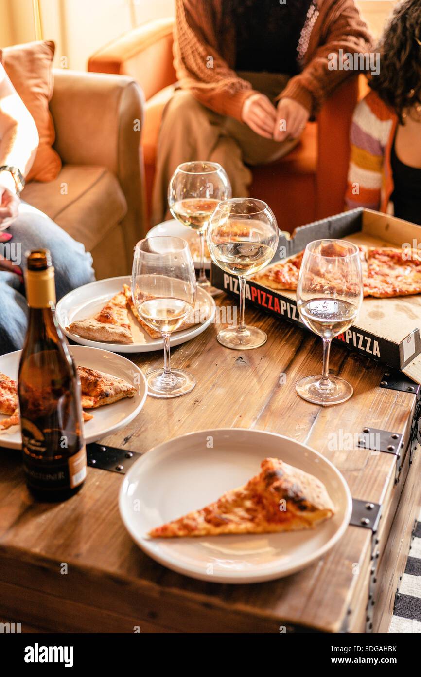 Freunde teilen sich Pizza und Weißwein an einem gemütlichen Wohnzimmertisch Stockfoto