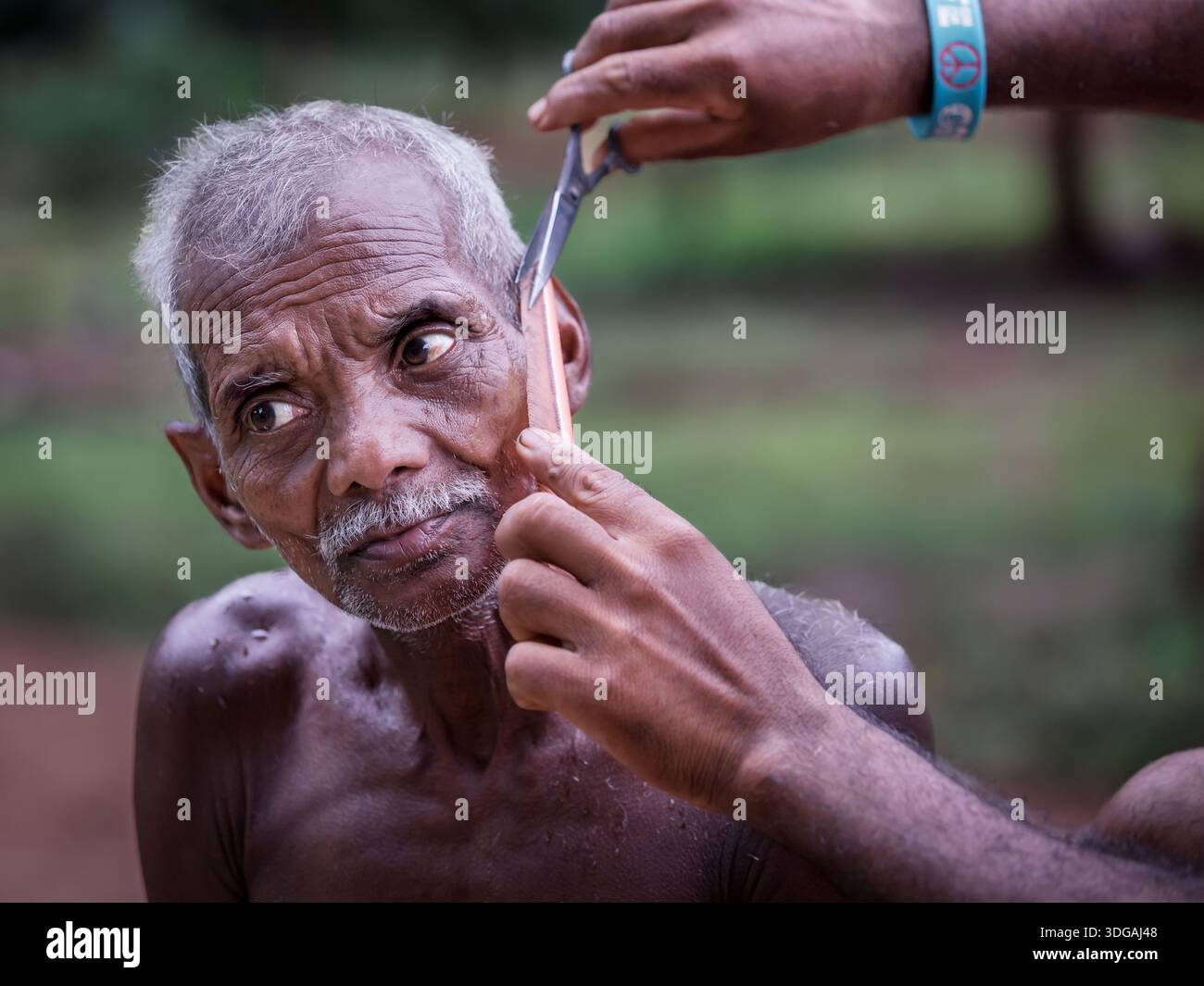 Ein älterer Indianer bekommt einen Haarschnitt, Odisha, Indien Stockfoto