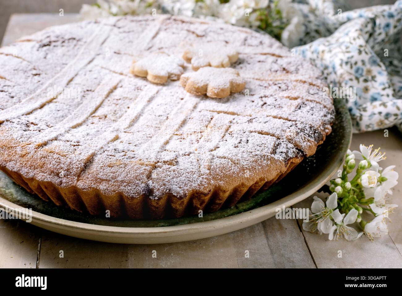 Köstlicher hausgemachter Pastiera Napolitano mit Puderzucker und Blumendekorationen oben. Serviert auf Keramikplatte mit weißer Feder Stockfoto