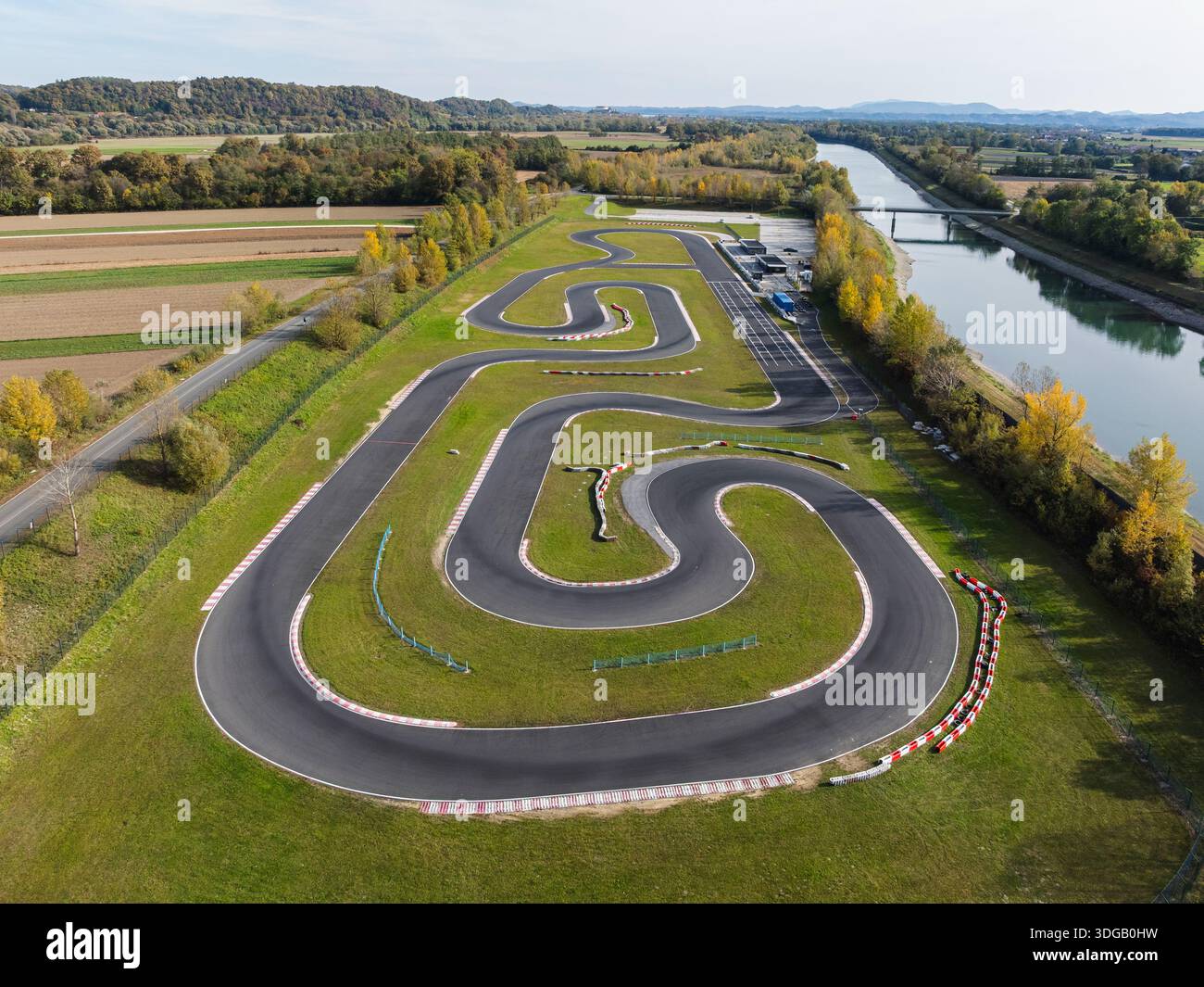 Aus der Vogelperspektive auf einer Kartstrecke, die sich durch Felder mit einem Fluss in der Nähe an einem klaren Tag unter blauem Himmel schlängelt. Stockfoto