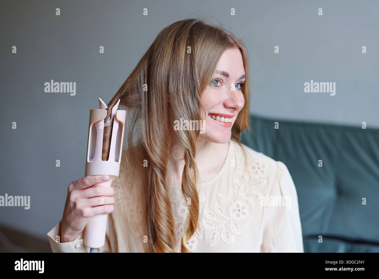 Junge Frau mit gesundem Haar mit Stylinggerät zu Hause, das moderne Schönheitsroutine repräsentiert Stockfoto