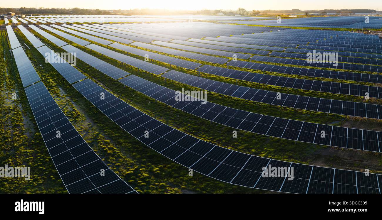 Luftpanorama aus Reihen von Photovoltaik-Solarpaneelen, die saubere und erneuerbare Energie auf landwirtschaftlichen Nutzflächen mit Sonnenuntergang und Kopien erzeugen Stockfoto