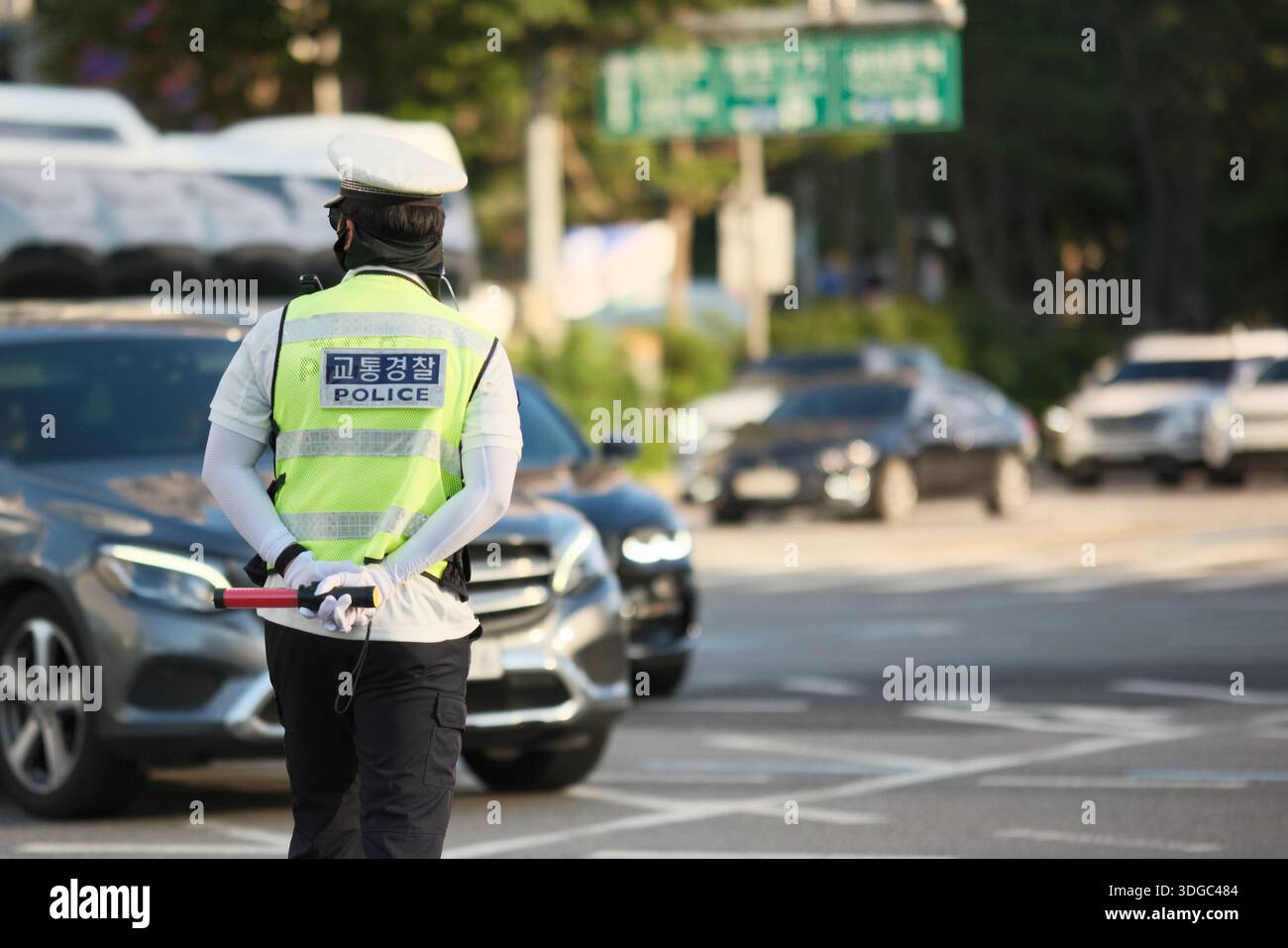 Seoul, Südkorea: Verkehrspolizist trägt eine reflektierende Weste und hält einen Schlagstock, während er Fahrzeuge an der geschäftigen Kreuzung kontrolliert Stockfoto