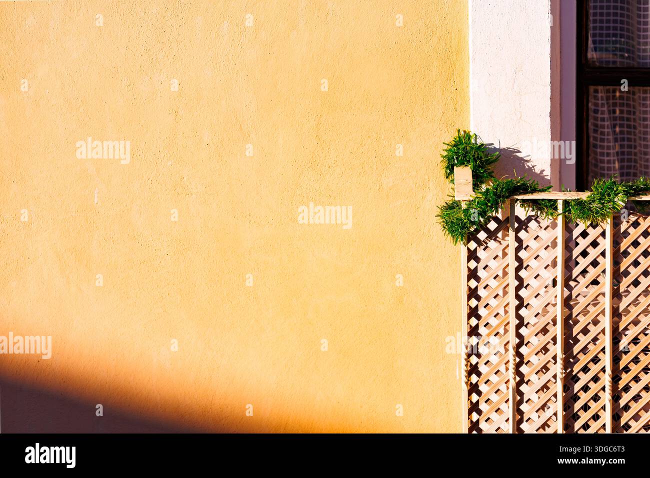 Eine breite, minimalistische Komposition einer gelb strukturierten Wand in Villajoyosa mit einem kleinen Teil eines dekorierten Balkons, der auf der rechten Seite sichtbar ist. Stockfoto