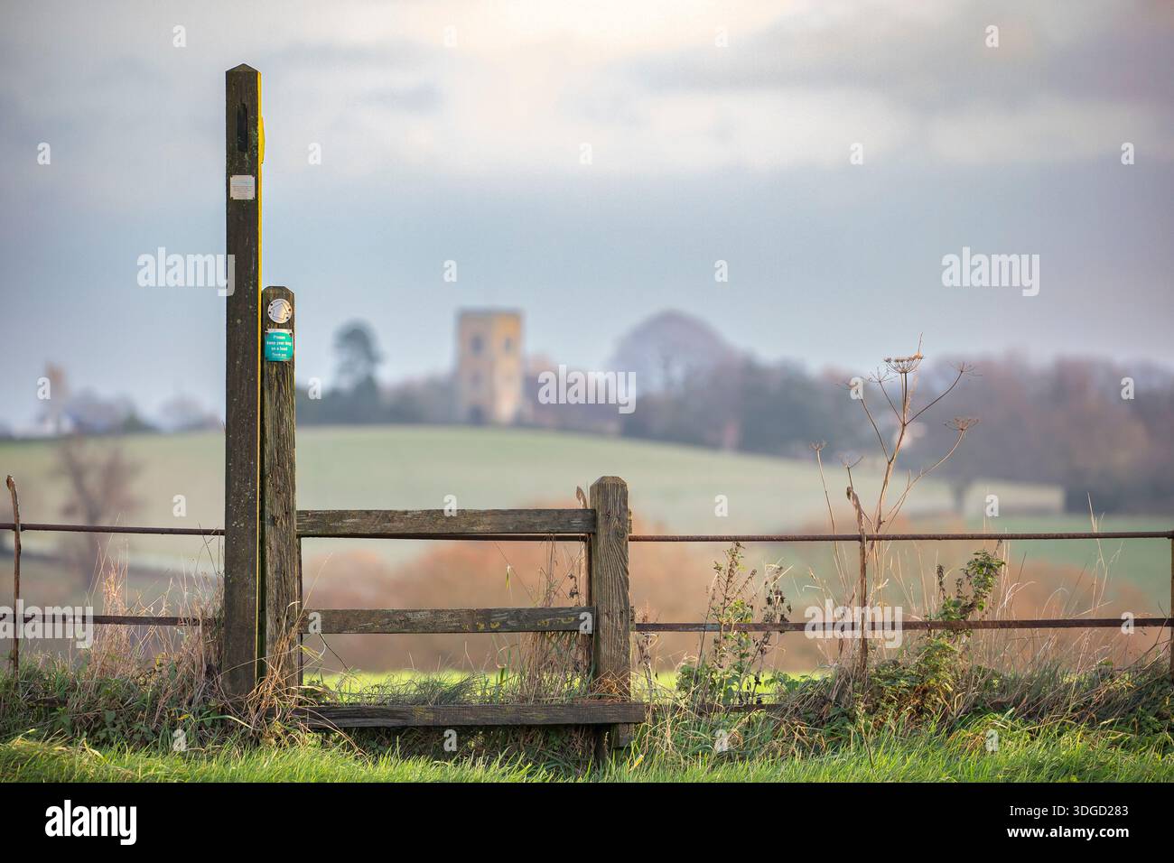 Fernansicht einer englischen Kirche über offene Landschaft und Felder mit einem Fußweg und einem Steg im Vordergrund. Stockfoto