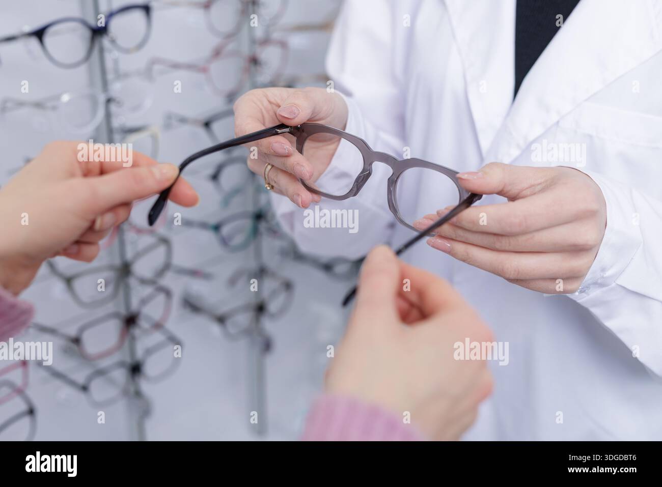Optiker in weißer Beschichtung bietet Brillenfassungen für Kunden in einem optischen Geschäft an. Geeignet für Website-Banner für Sehpflege, Brillenwerbung und Klinikprofi Stockfoto