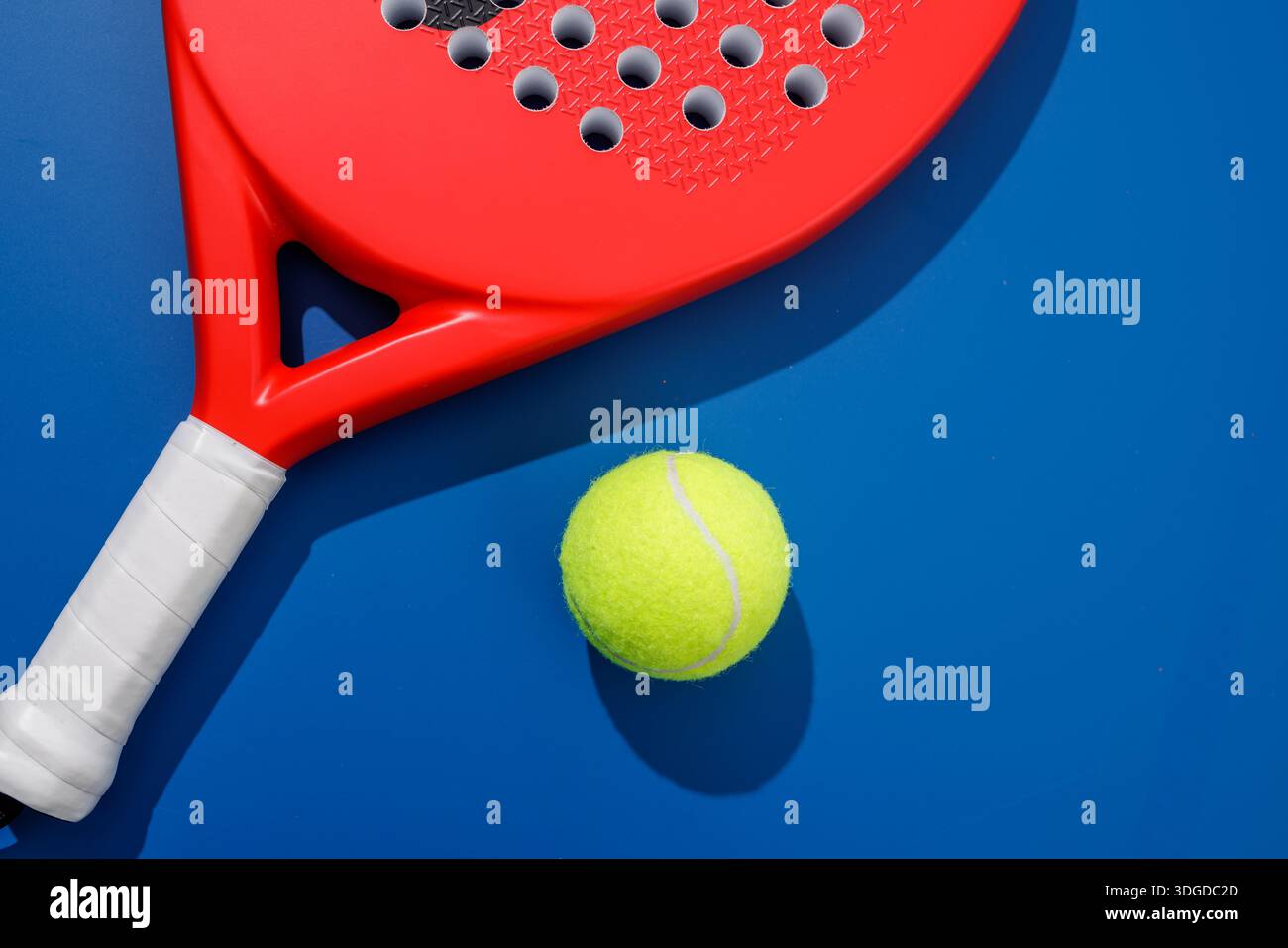 Kurzer Padel-Schläger und gelber Ball auf blauem Platz mit starkem Schatten für Design und Trainingskonzept für Sportbanner Stockfoto