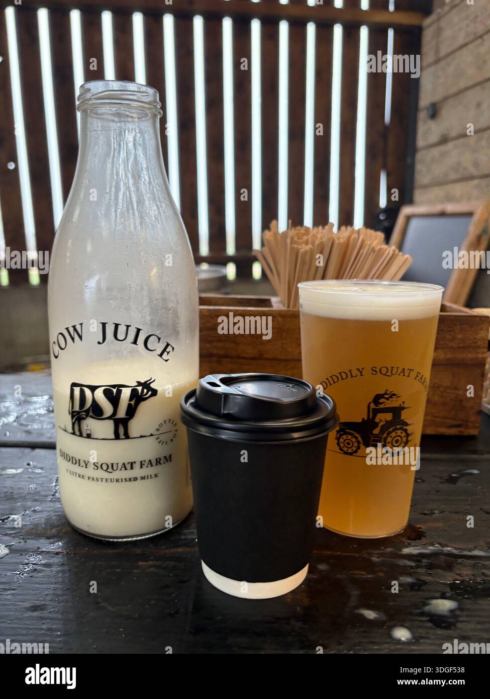 Frische Bauernmilchflasche, Kaffeetasse zum Mitnehmen und Craft-Bier auf rustikalem Holztisch im Landhauscafé Diddly Squat Stockfoto