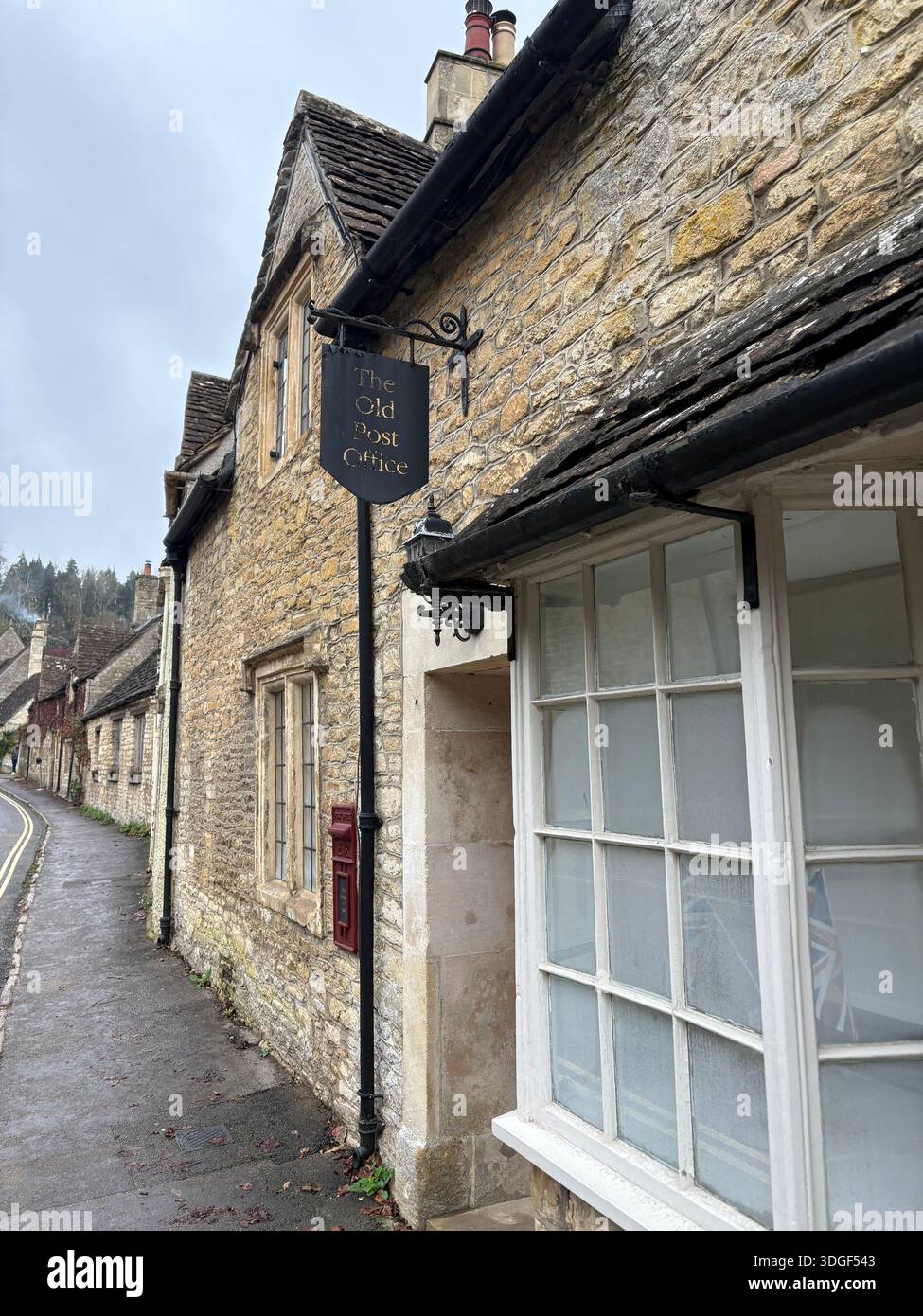 Traditionelles Steingebäude mit Ladenschild entlang einer engen Straße in Burford, einer historischen Stadt der Cotswolds in England, an einem bewölkten Tag. - Smartphone-aufgenommenes Stockfoto