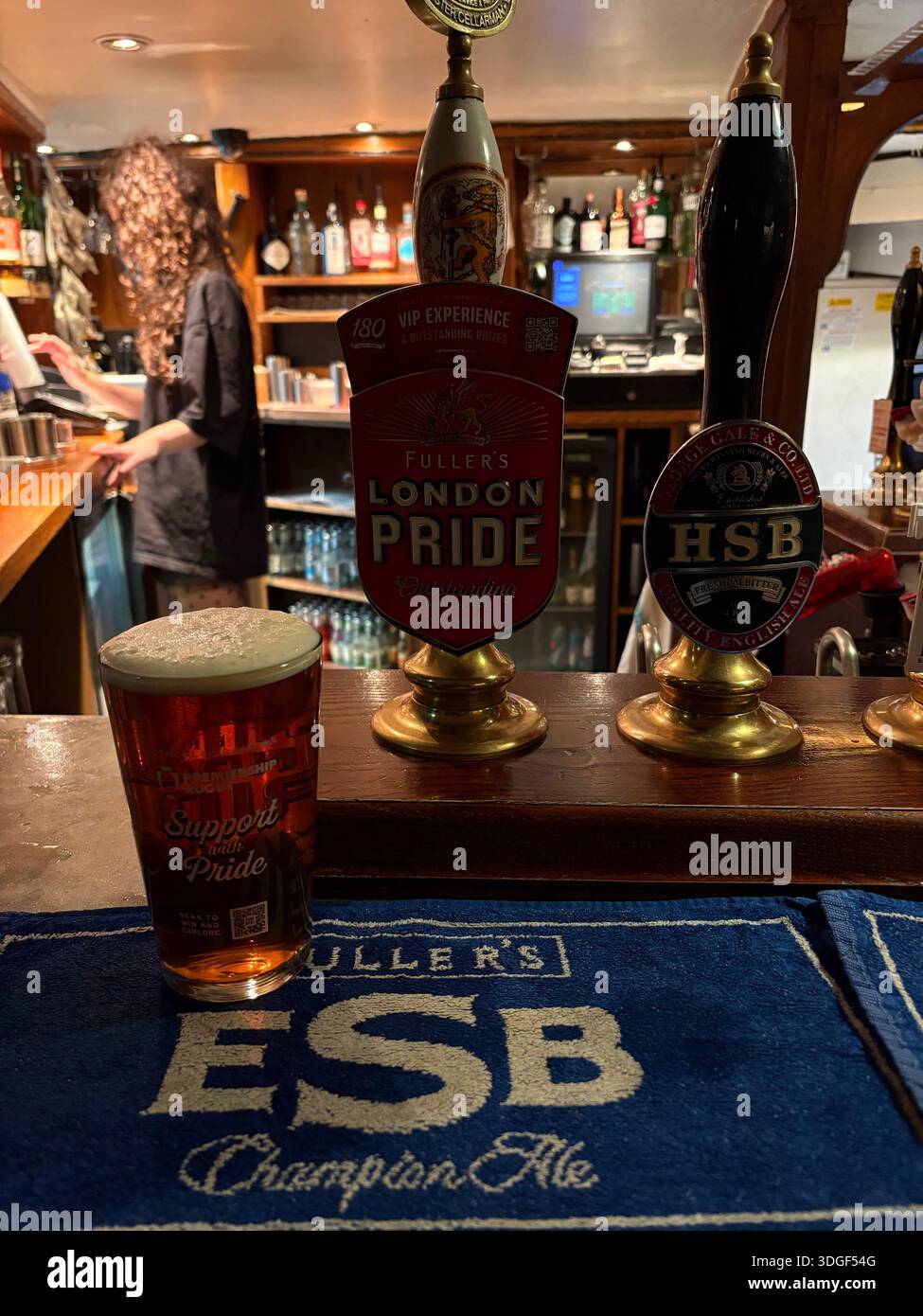 Ein Bier auf einem Pub mit traditionellen britischen Bierpumpengriffen und Barkeeper im Hintergrund in einem klassischen englischen Pub. - Smartphone-aufgenommenes Stockfoto