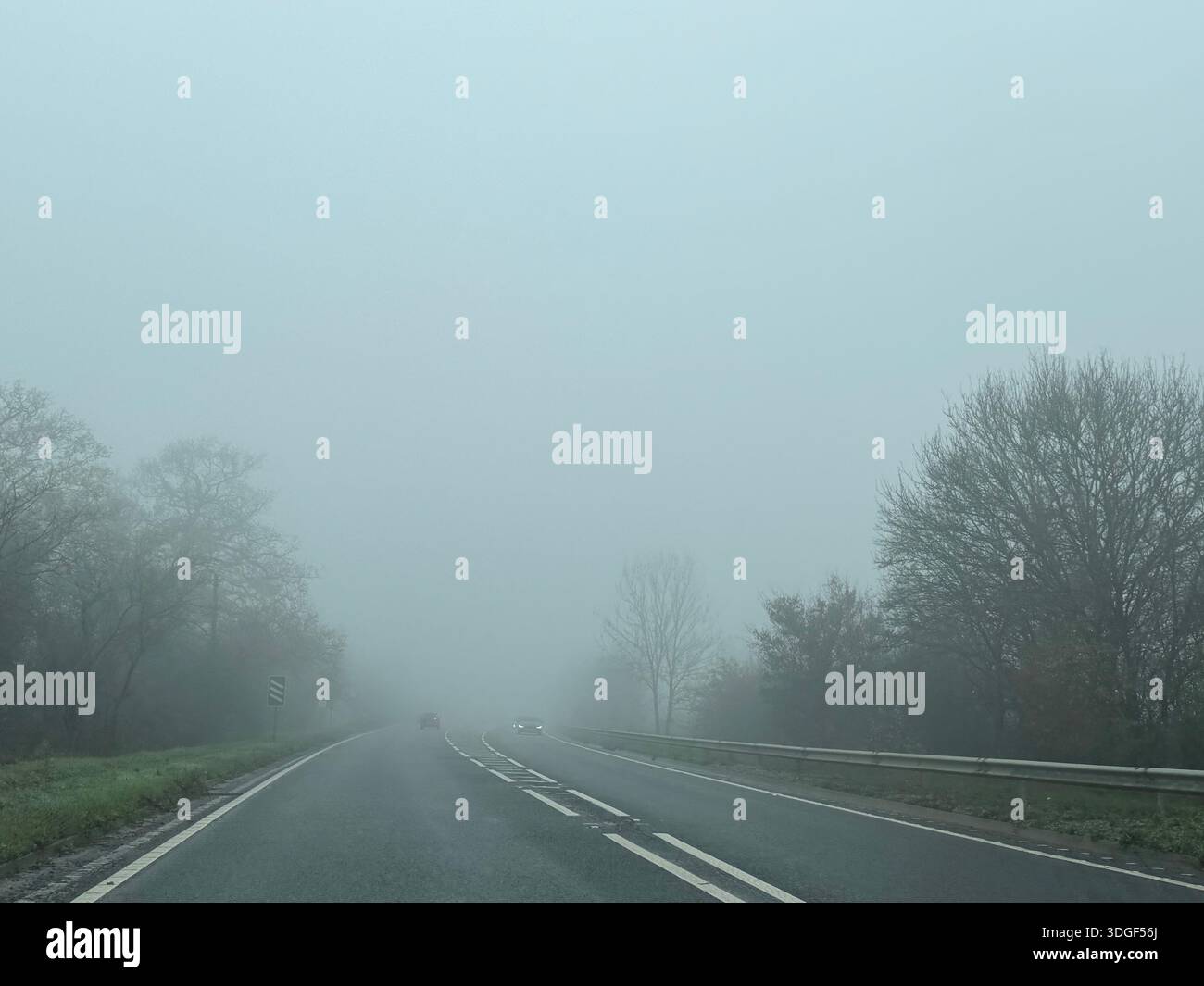 Nebelige Landstraße mit geringer Sicht und weit entfernte Autos fahren durch dicken Nebel und schaffen eine stimmungsvolle und atmosphärische Wetterszene. Stockfoto
