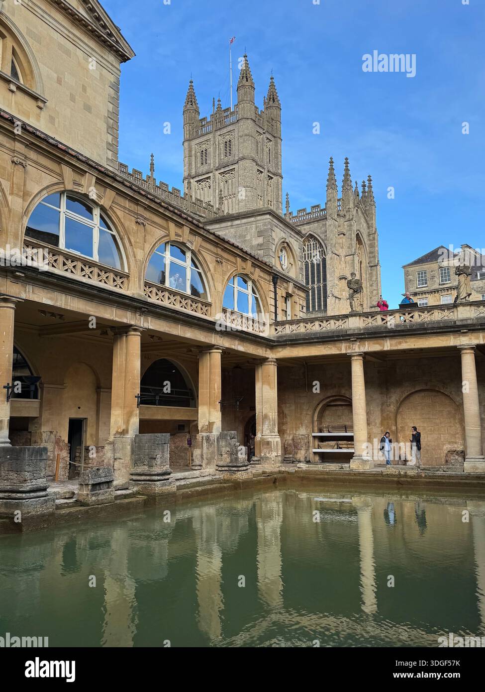 Der Innenhof der römischen Bäder mit reflektierendem Pool und historischen Steinkolonnaden, über dem sich Bath Abbey erhebt, England. - Smartphone-aufgenommenes Stockfoto