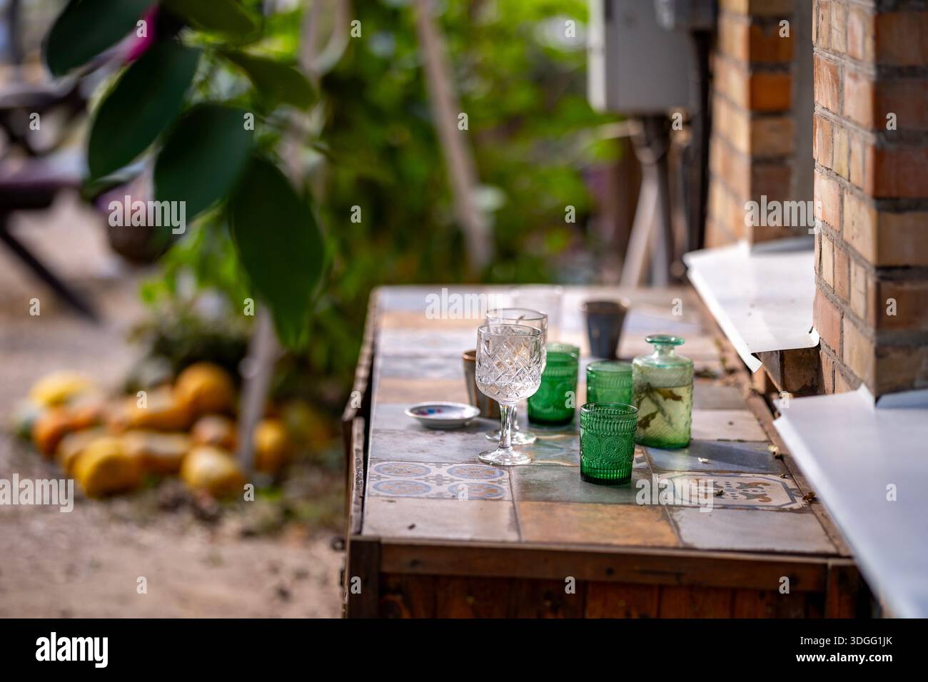 Ein Tisch auf der Sommerterrasse eines Cafés bietet eine Auswahl an Gläsern und Tassen, darunter elegante Stielgläser und verschiedene grüne Gläser, mit b Stockfoto