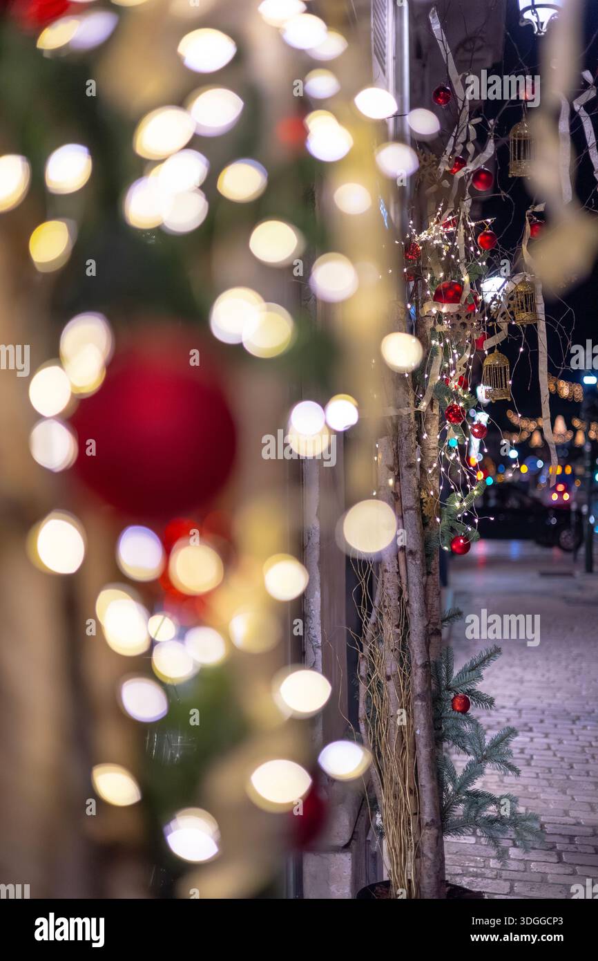 Vertikale Nachtansicht auf Weihnachtsdekorationen mit roten Ornamenten und warmweißen Lichtern mit schwerem Bokeh aus einer verschwommenen Stadtstraße und Autolichtern Stockfoto