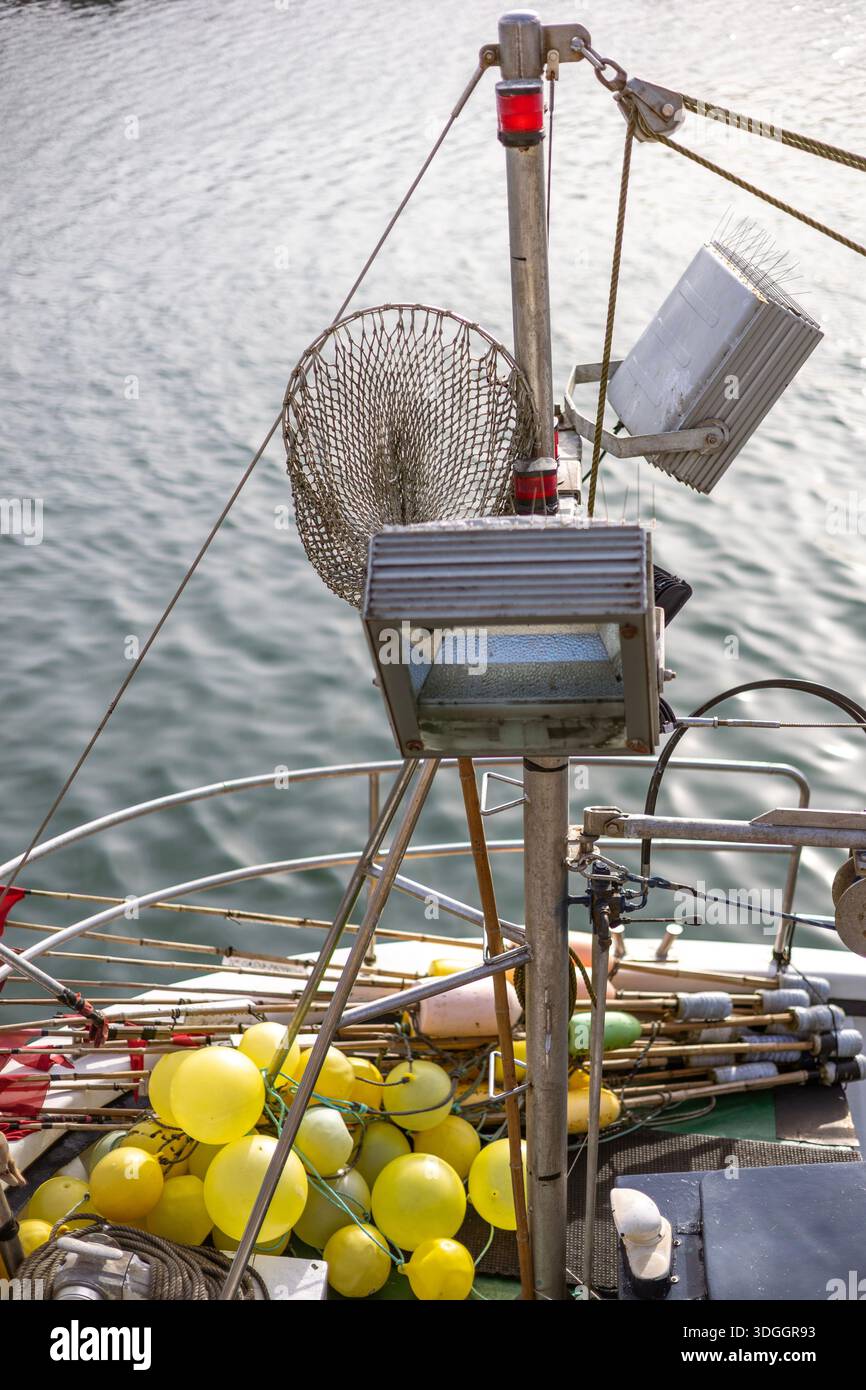 Nahaufnahme des Mastes und Deck eines Fischerbootes. Zur Ausstattung gehören Decklichter, ein Tauchnetz und ein Haufen von gelben Bojen und Schwimmern auf dem Deck darunter. Stockfoto