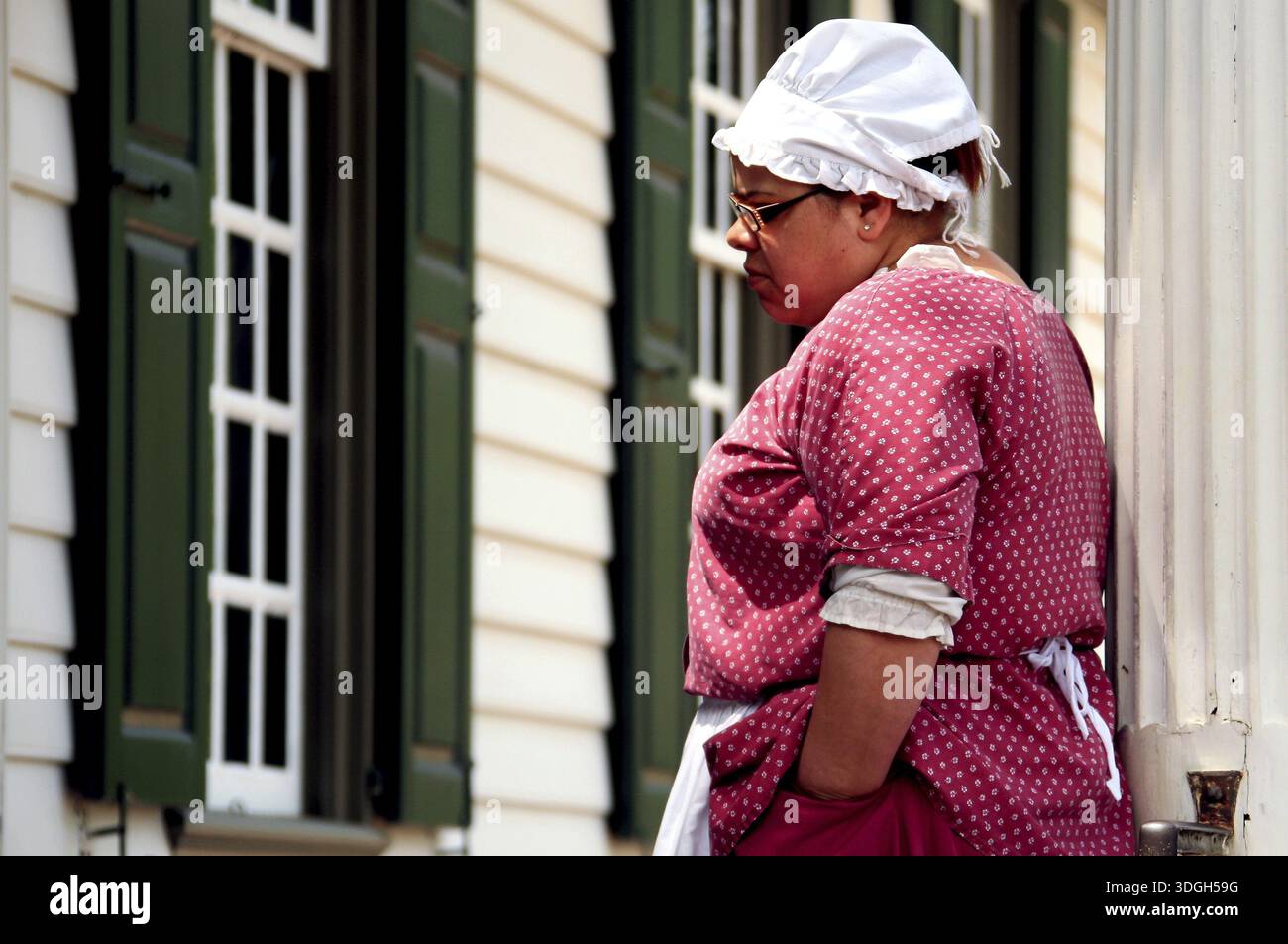 Frau in zeitgenössischer Kleidung, die sich ein Gebäude in Colonial Williamsburg ansieht, ein Eindruck aus der Kolonialzeit, Williamsburg, Virginia, USA Stockfoto