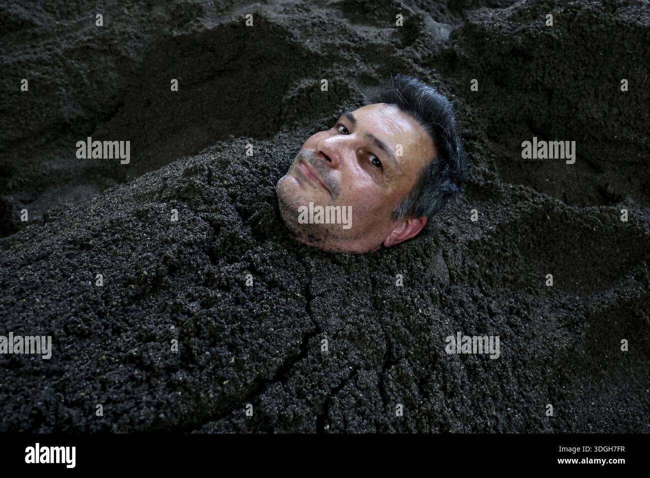 Mann im Sandbad begraben, nur der Kopf nach oben, entspannter Ausdruck, Beppu, Takegawara Onsen, Japan Stockfoto