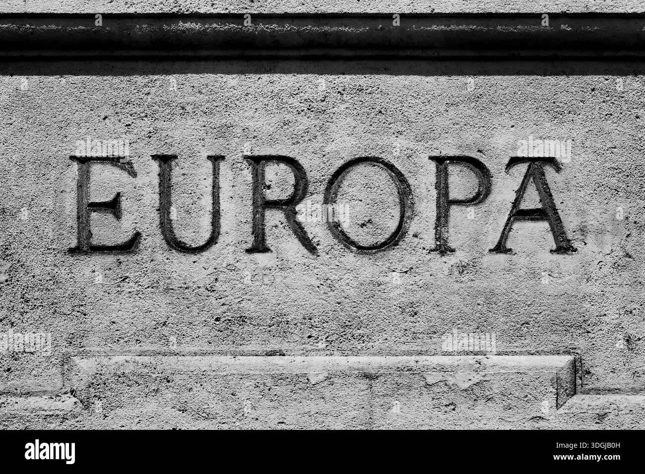 Ein Nahaufnahme, Schwarzweiß-Foto des Wortes „Europa“, das in einem klassischen Serifenschriftstein in ein Steindenkmal geschnitzt wurde. Ein strukturiertes Bild erzeugt ein leistungsstarkes an Stockfoto