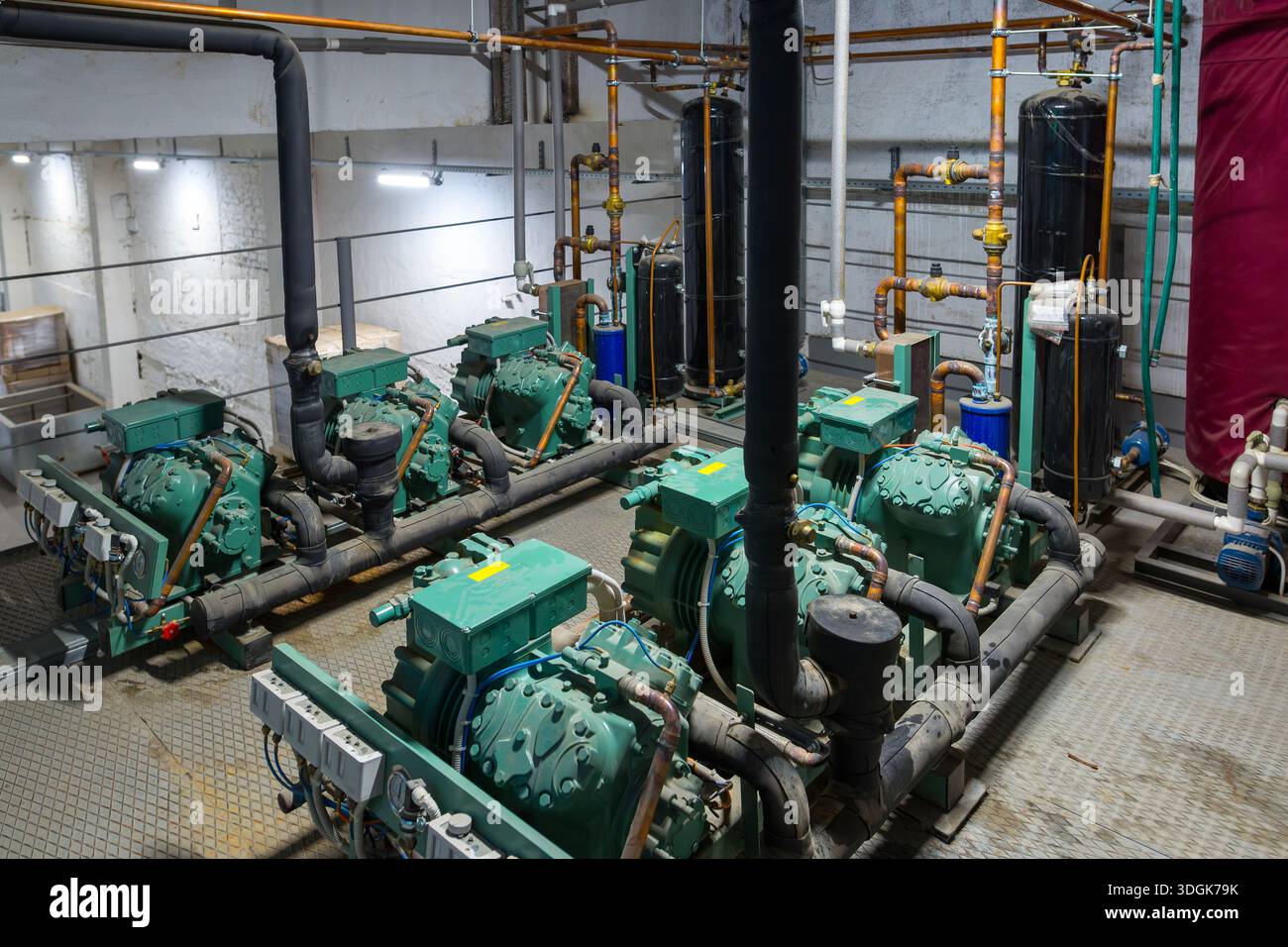 Der Industriekühlerraum. Mehrere grüne halbhermetische Kompressoren sind an ein System aus Kupfer- und isolierten Rohren, Tanks und Manometer angeschlossen Stockfoto