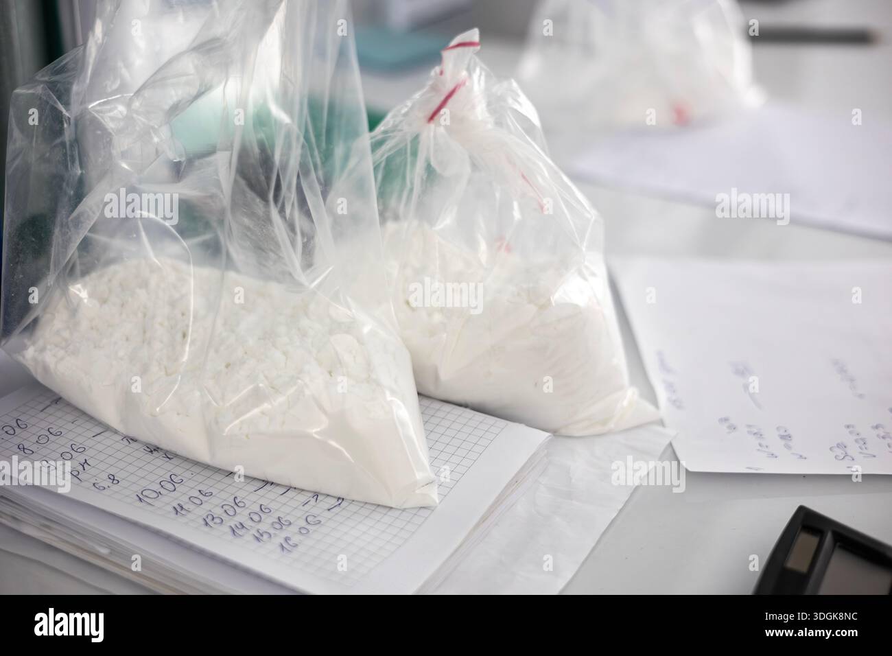 Drei durchsichtige Plastikbeutel, gefüllt mit einem unbekannten weißen Pulver oder einer kristallinen Substanz, sitzen auf einem Schreibtisch. Die Taschen sind auf Papieren mit handgeschriebenem Nein Stockfoto