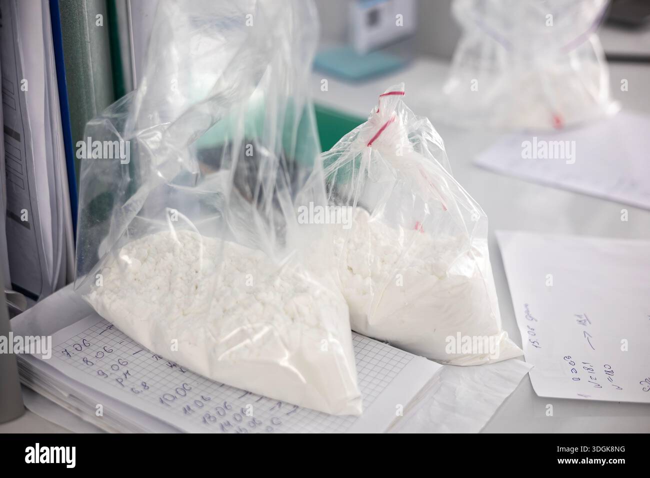 Drei durchsichtige Plastikbeutel, gefüllt mit einem unbekannten weißen Pulver oder einer kristallinen Substanz, sitzen auf einem Schreibtisch. Die Taschen sind auf Papieren mit handgeschriebenem Nein Stockfoto