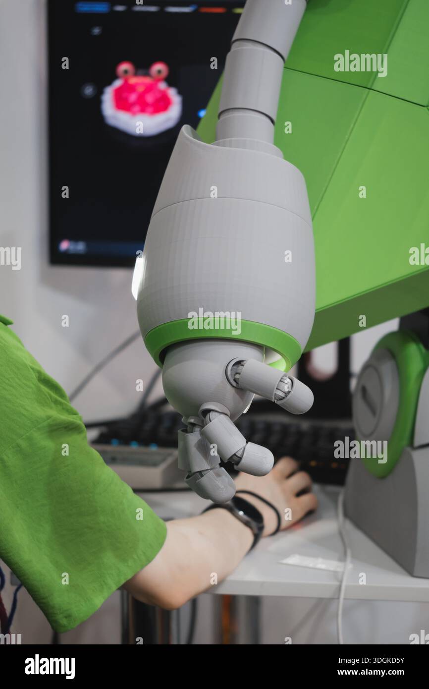 Frau und humanoider Roboterarm mit beweglichen Fingern über dem Computerpult im modernen technischen Arbeitsbereich, arbeiten zusammen, spielen und bedienen Stockfoto