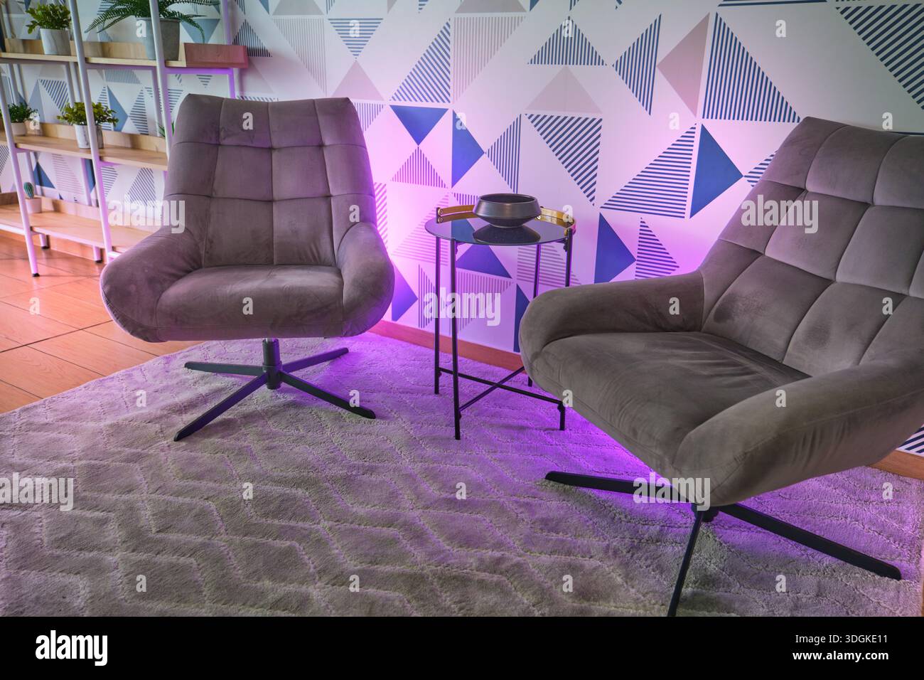 Zwei moderne Sessel sitzen auf einem Teppich in einem Wohnbereich mit geometrischer Tapete Stockfoto