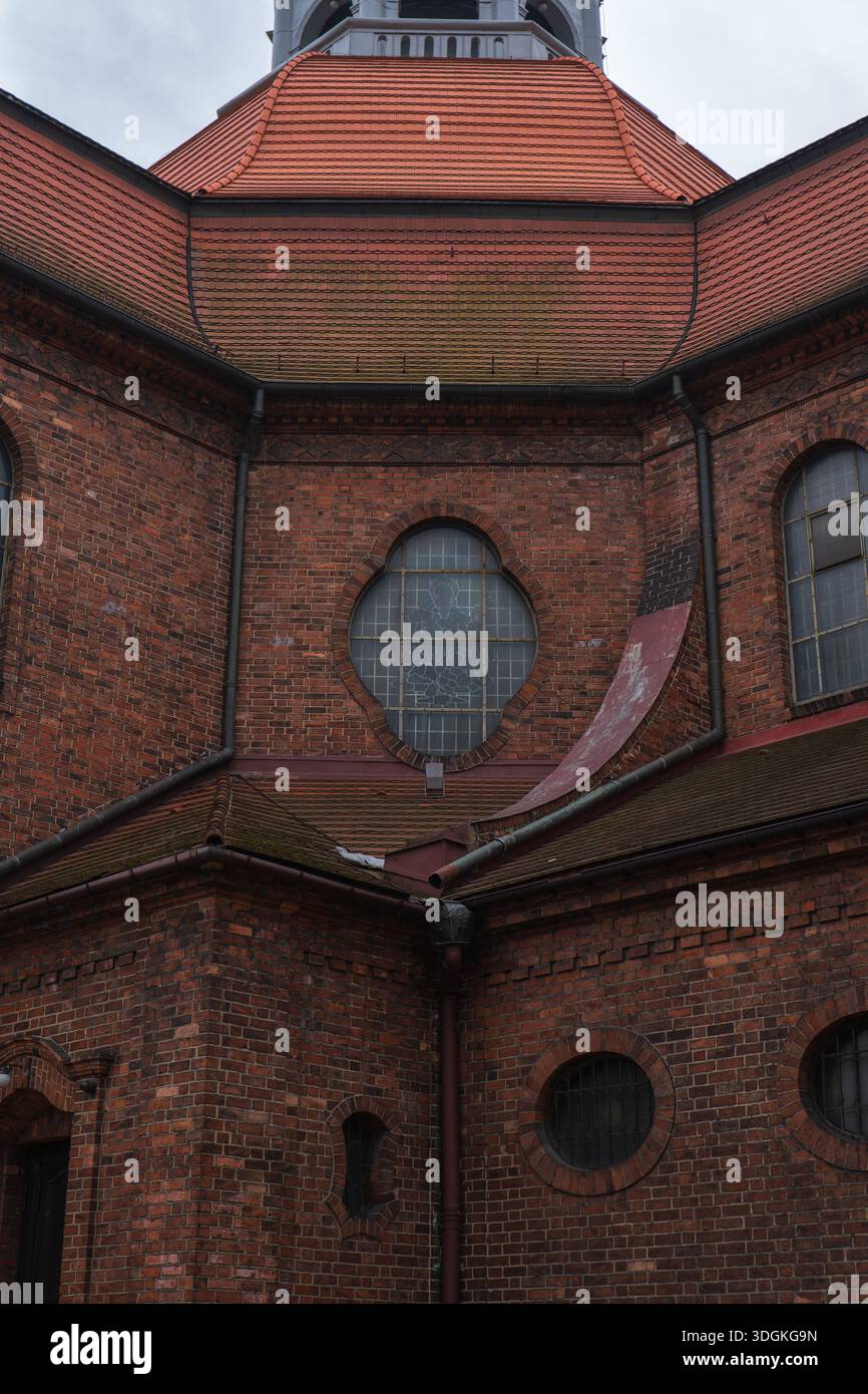 Die rote Backsteinfassade in Kattowitz zeigt ein achteckiges Dach mit orangefarbenen Fliesen, ein viereckiges Fenster mit gemustertem Glas, Eisengitter, Dachrinnen und wir Stockfoto