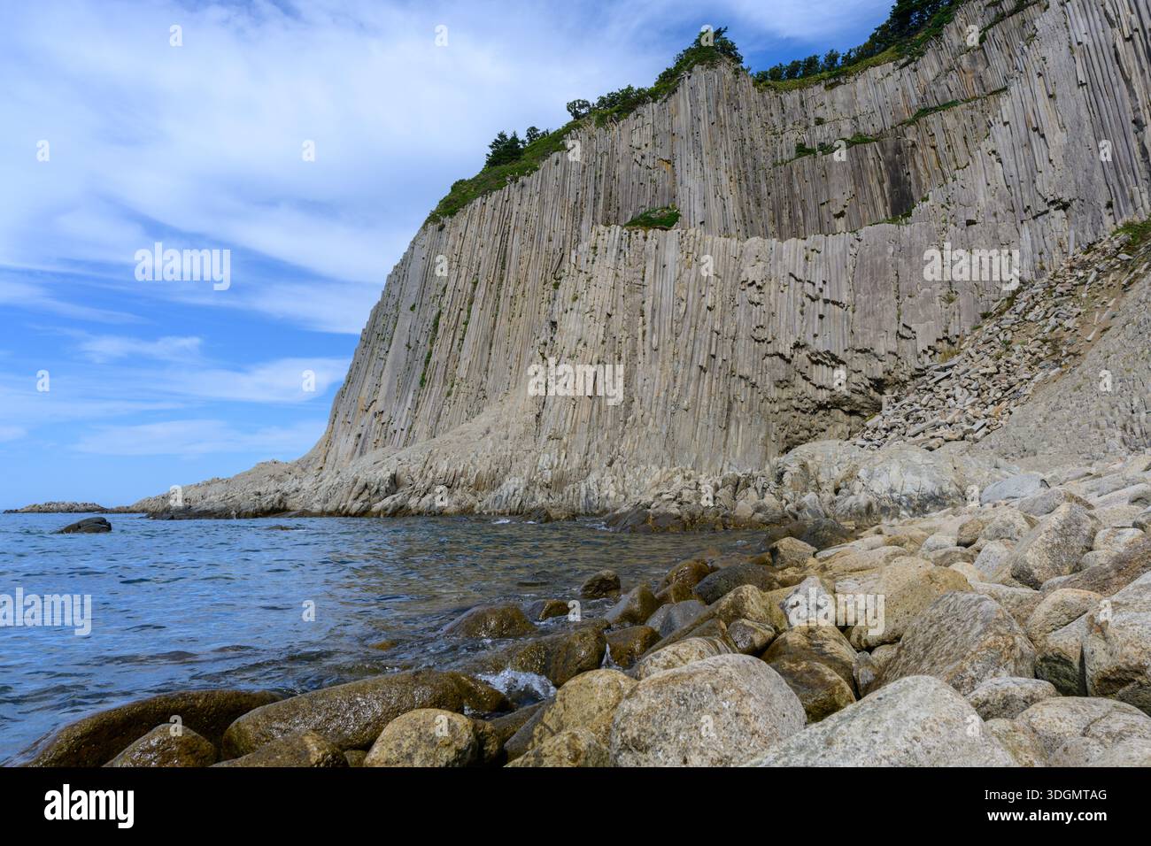 Hohe Klippen mit einzigartigen kantigen Formationen ragen an einem friedlichen Tag in Russland über das ruhige Meer. Die felsige Küste ist mit glatten Steinen und c Stockfoto