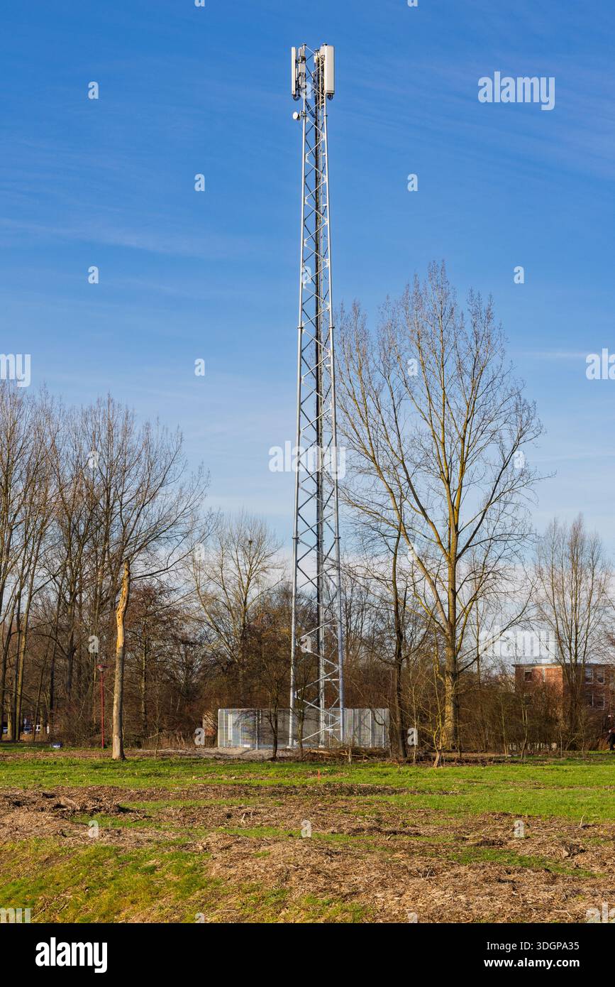 Hoher Telekommunikationsturm aus Stahl oder Mobilfunkmast, der an einem sonnigen Tag senkrecht in einem grünen Park mit Bäumen vor einem klaren blauen Himmel steht. Stockfoto