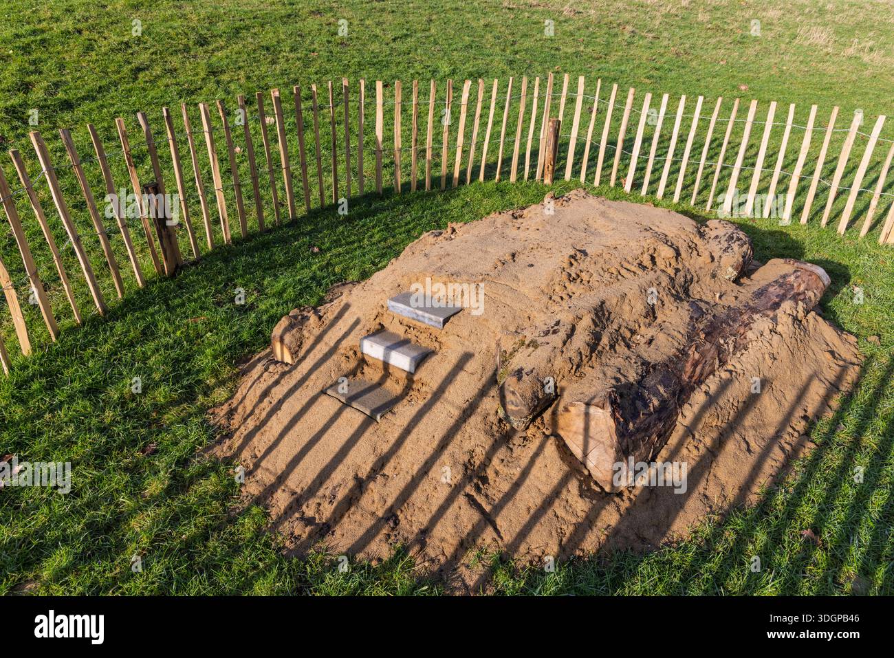 Sandiger Bienenhügel mit Holzstämmen und Stufen, die von einem Zaun in einem grünen Park umgeben sind und als Brutstätte für Wildbienen und Biodiversität konzipiert wurden. Stockfoto