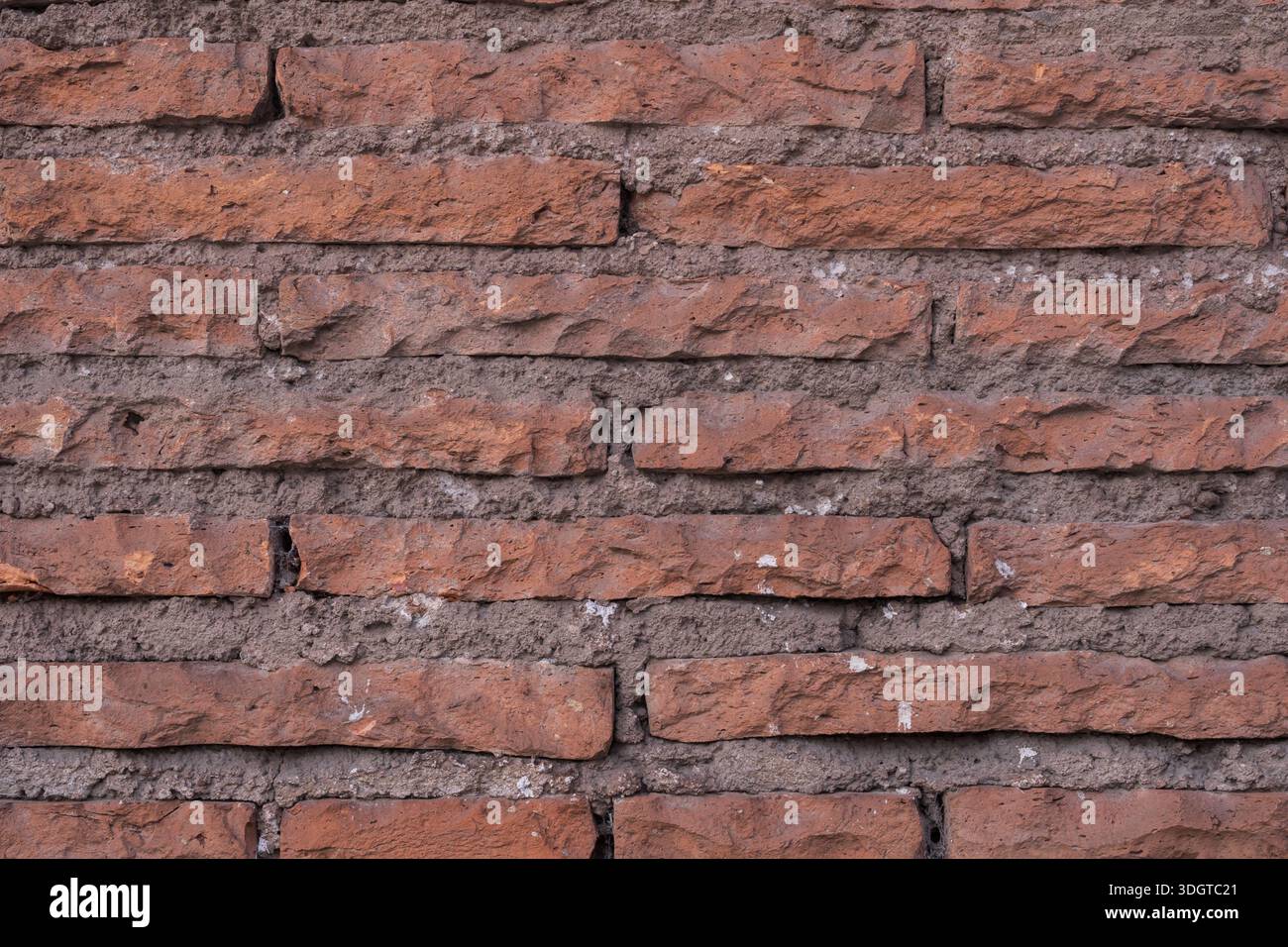 Alte rote Ziegelwand mit rauer Textur, unebenen Ziegeln und abgenutztem Mörtel. Architektonischer Hintergrund mit einem natürlichen und authentischen urbanen Look. Stockfoto