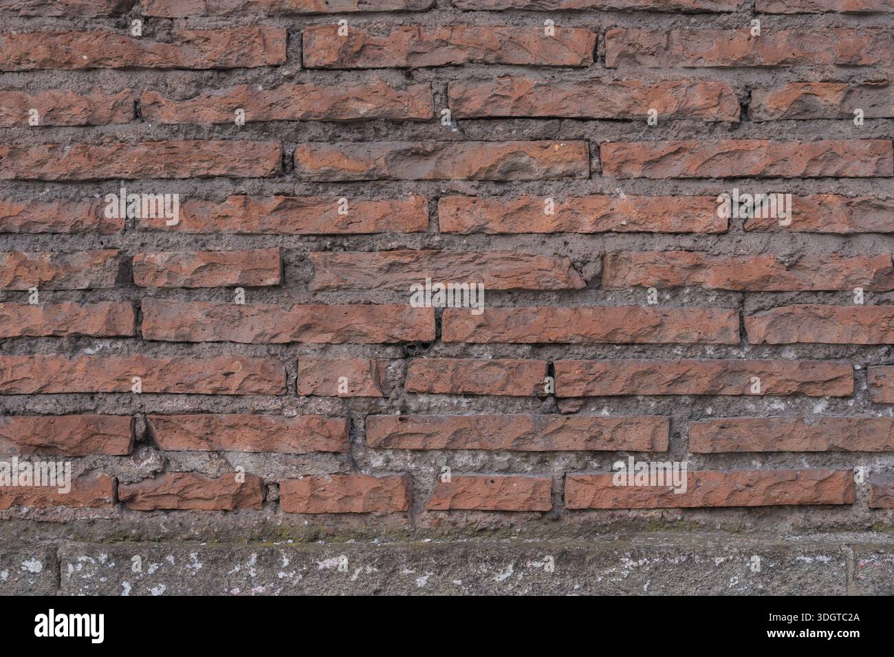 Alte rote Ziegelwand mit rauer Textur, unebenen Ziegeln und abgenutztem Mörtel. Architektonischer Hintergrund mit einem natürlichen und authentischen urbanen Look. Stockfoto