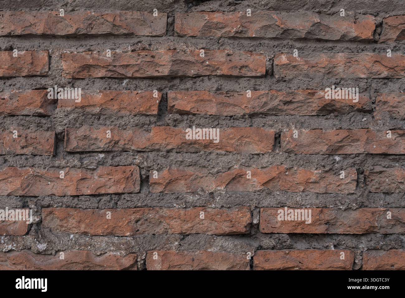 Alte rote Ziegelwand mit rauer Textur, unebenen Ziegeln und abgenutztem Mörtel. Architektonischer Hintergrund mit einem natürlichen und authentischen urbanen Look. Stockfoto