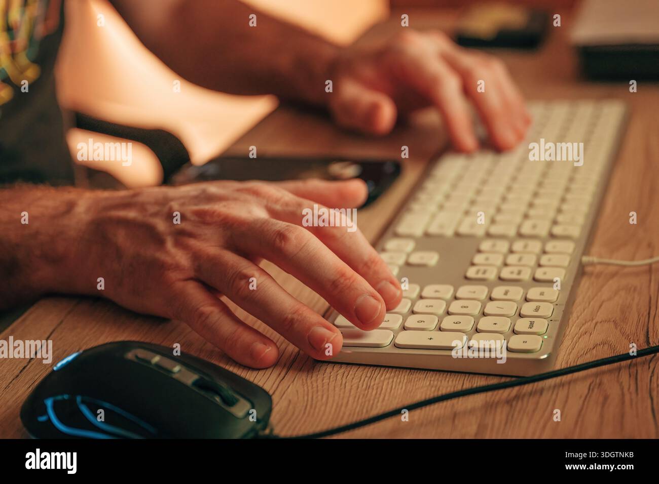 Nahaufnahme männlicher Hände, die mit Maus und Smartphone auf der Computertastatur tippen, selektiver Fokus Stockfoto