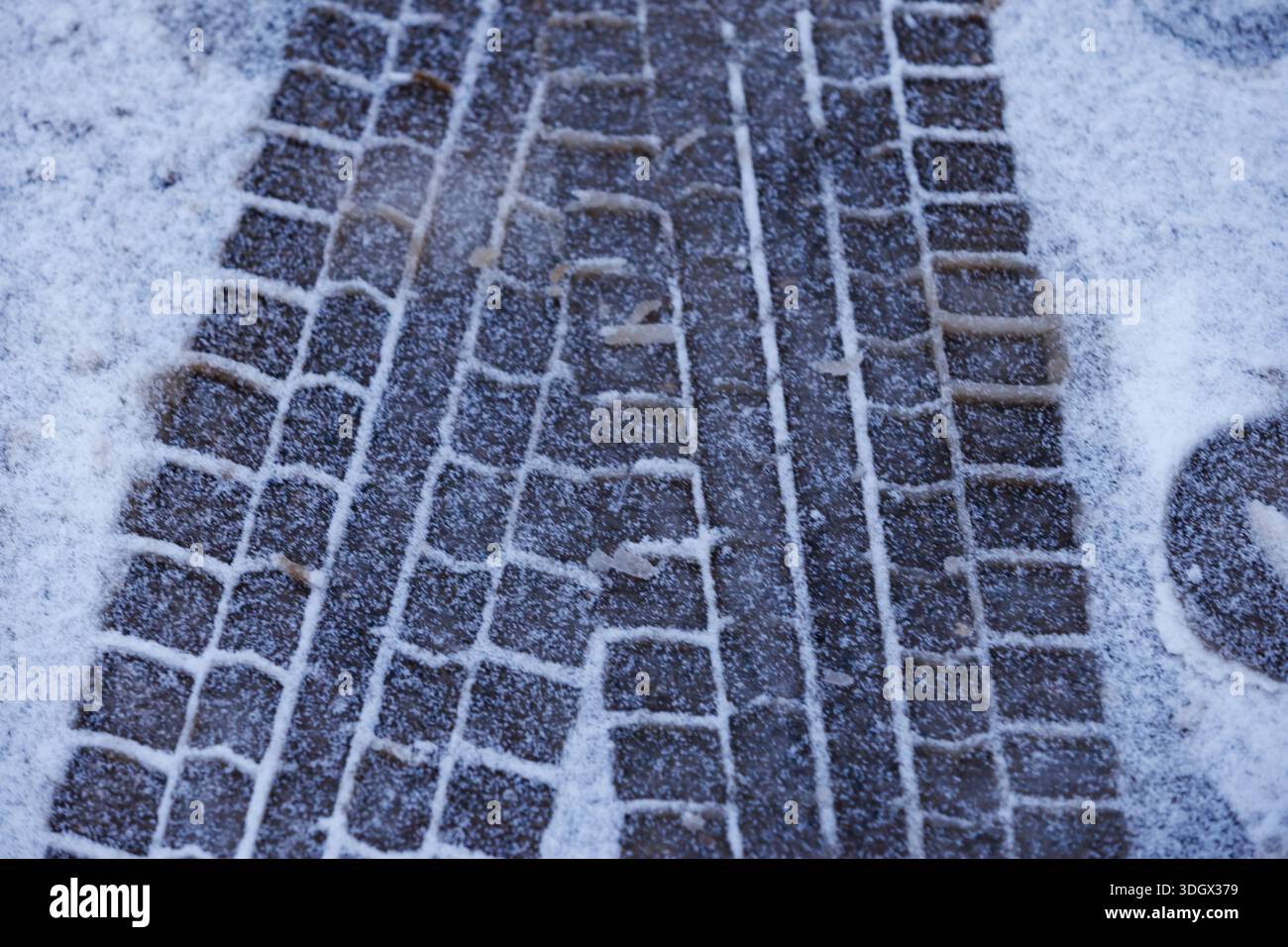Reifenspuren auf Neuschnee. Nahaufnahme von Pkw-Reifenspuren, die in Neuschnee auf dem Straßenbelag eingeprägt sind, winterliche Straßenbeschaffenheit und Transportkonzept. Stockfoto