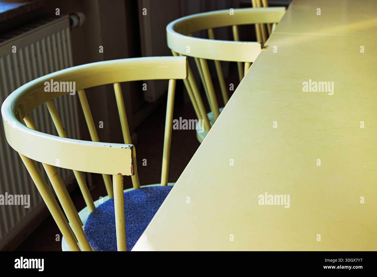 Leere gelbe Stühle neben dem Tisch in der sonnendurchfluteten Küche mit großer Tischplatte, die Platz zum Kopieren bietet. Stockfoto