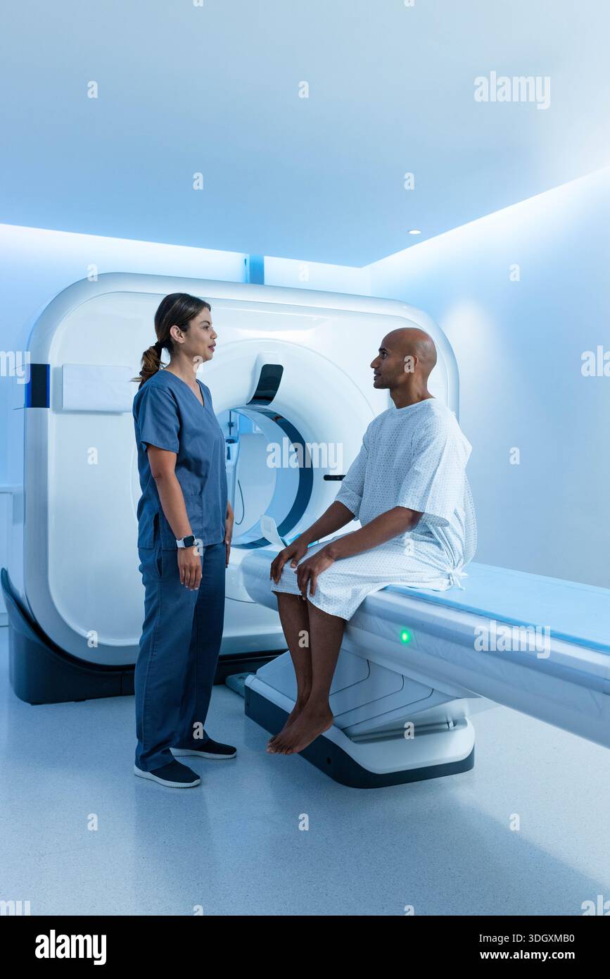 Afroamerikanischer Kliniker Marine-schrubbt mit einem Patienten, der auf einem CT-Tisch sitzt, im Kleid in der Nähe der Gantry Stockfoto