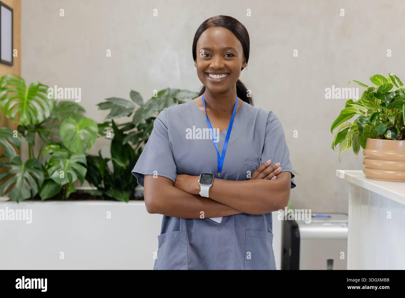 Afroamerikanerin, die am Empfang der Klinik steht, trägt graue Peelings, Schlüsselband und Smartwatch Stockfoto