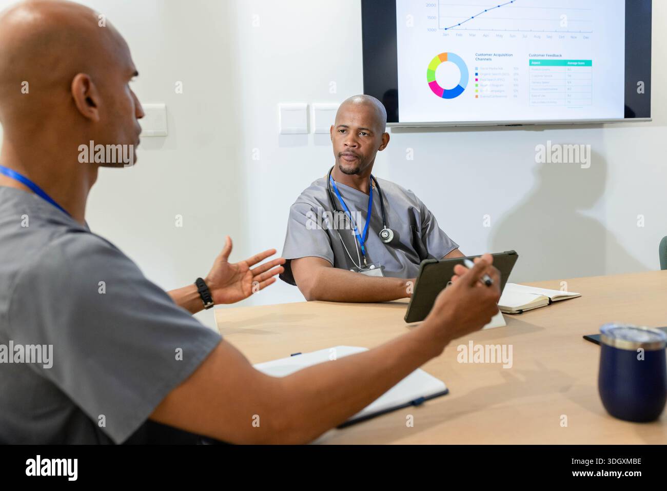 Afroamerikanische männliche Kollegen in Scrubs diskutieren Diagramme auf Tablette mit Stethoskop in der Klinik Stockfoto