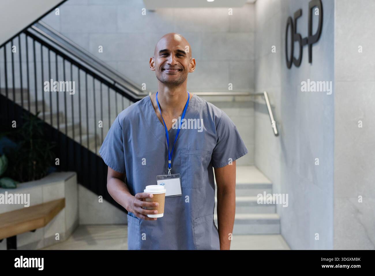 Afroamerikanischer Mann, der in der Lobby steht und eine Kaffeetasse hält und graue Gestrüpp mit Schlüsselband trägt Stockfoto