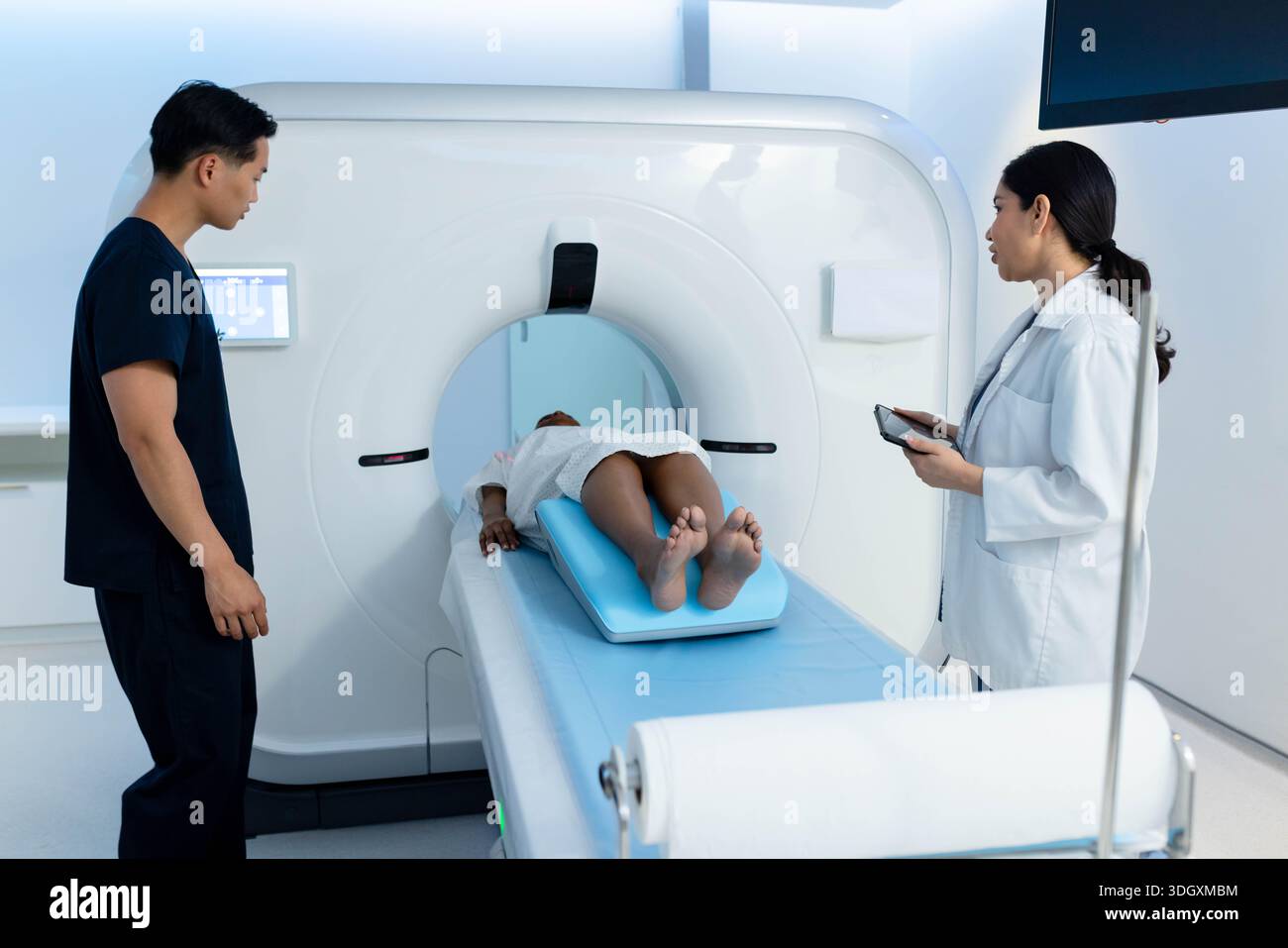 Verschiedene medizinische Teams positionieren den Patienten auf dem Pad im CT-Raum, Arzt im Laborkittel mit Tablette Stockfoto