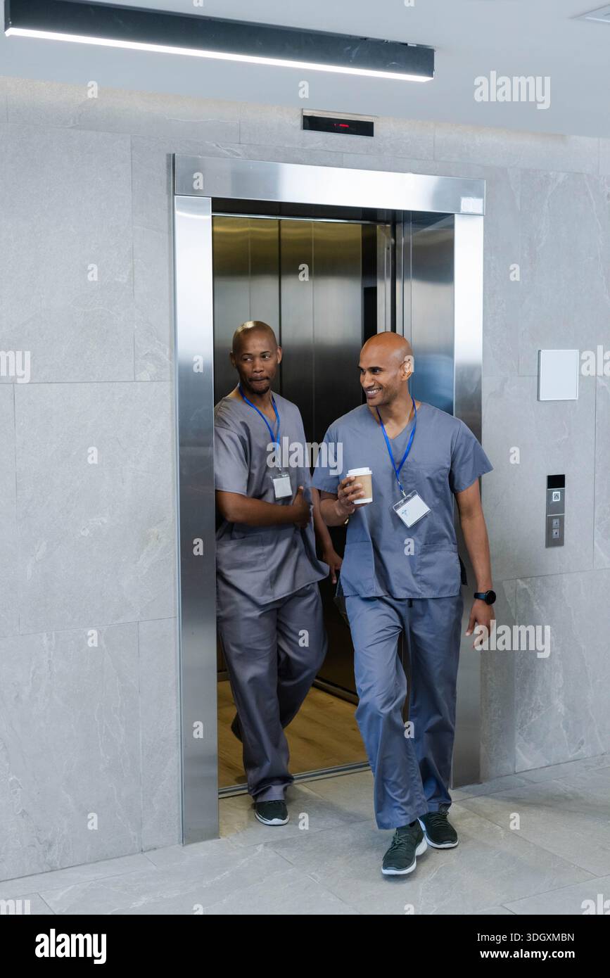 Afroamerikanische Männer, die aus dem Metall-Lift gehen, tragen blaue Peelings mit Ausweisschildern, einer mit Kaffee Stockfoto