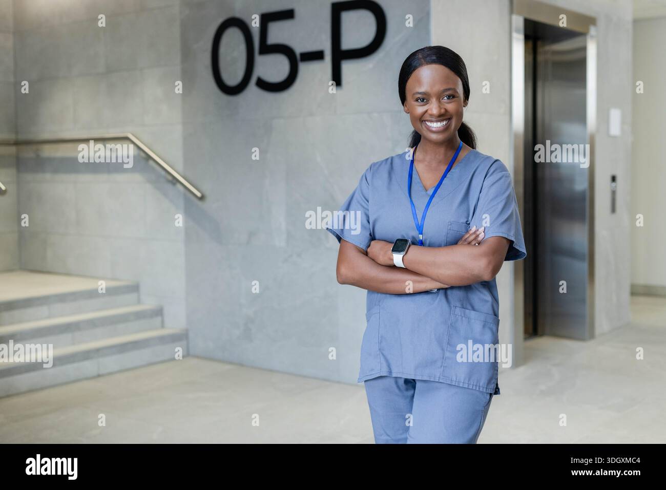 Weibliche Krankenschwester lächelt in der Nähe des Fahrstuhls, Schild mit 05-P-Zeichen in der Lobby, blaue Schürzen, Ausweis, Kopierraum Stockfoto