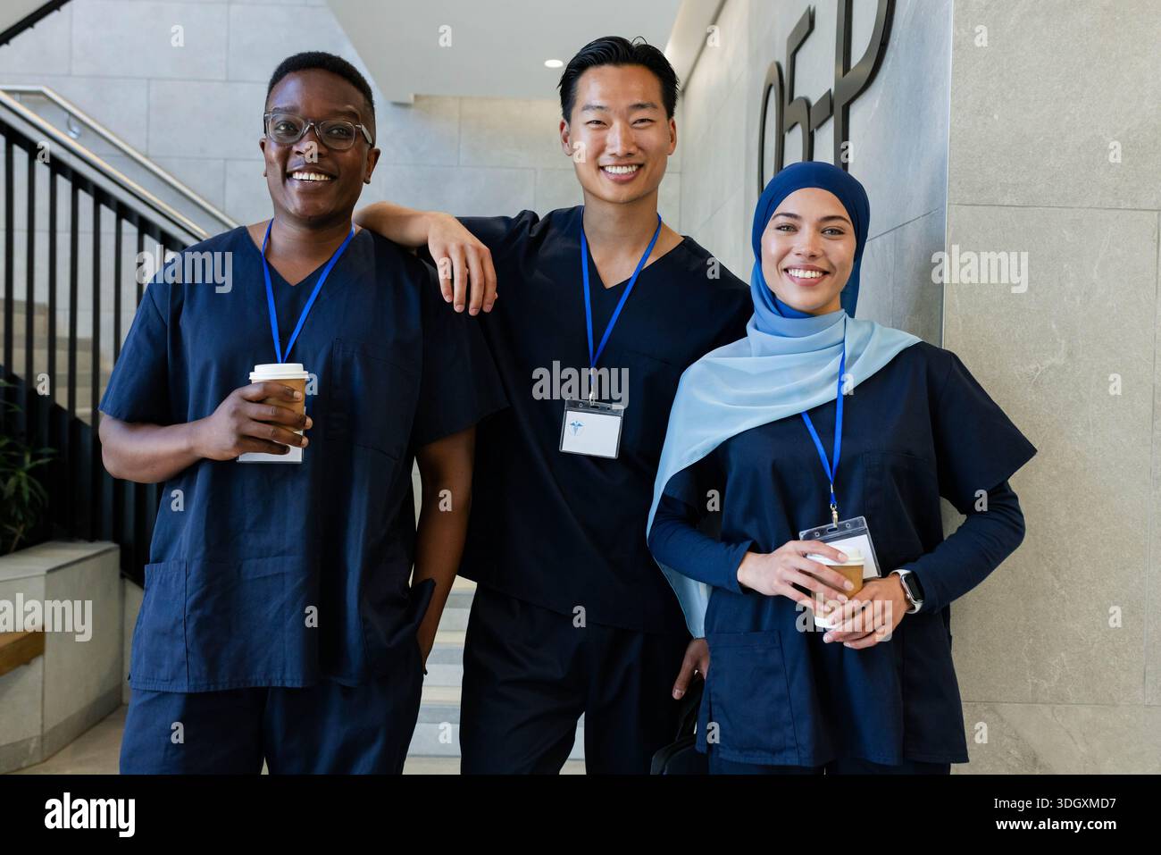 Diverse medizinische Teams, die marineblaue Peelings auf den Treppen im Krankenhaus tragen und Kaffee und blaue Lanyards halten Stockfoto