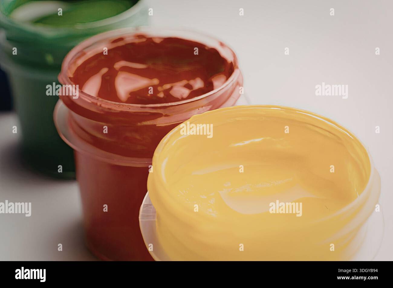 Ein Bild mit drei offenen Farbgläsern in leuchtenden Farben, darunter Grün, Rot und Gelb, die auf einer Oberfläche angeordnet sind. Stockfoto